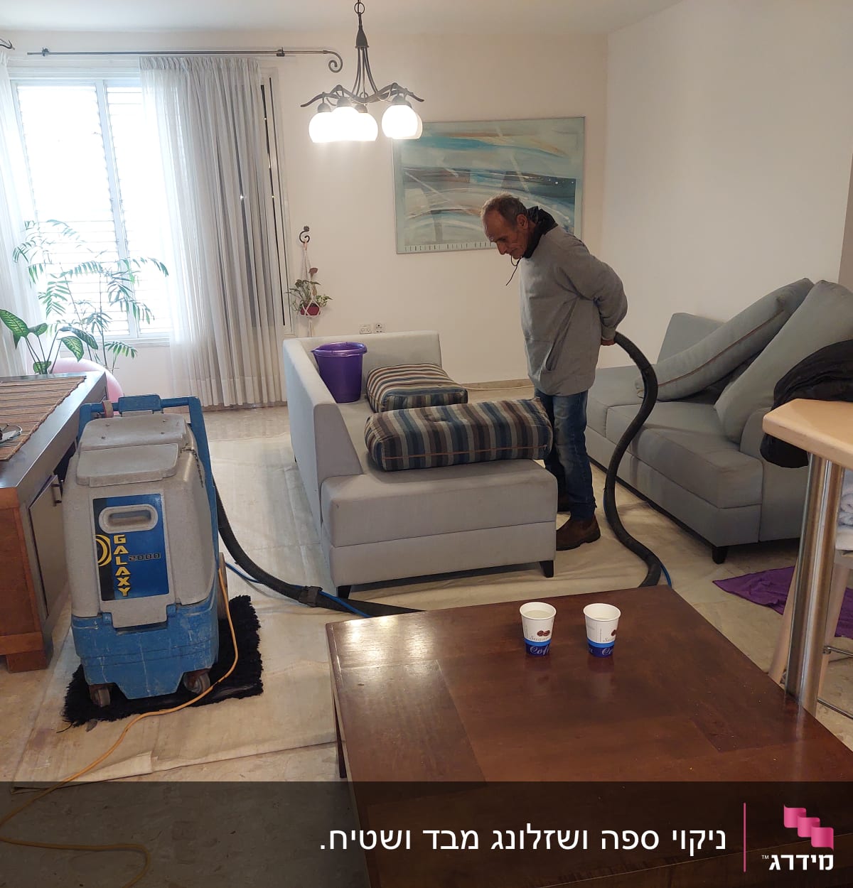 אדם מנקה ספה עם מכונת ניקוי מקצועית